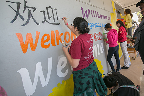 Students painting a wall with Welcome written on it in various languages